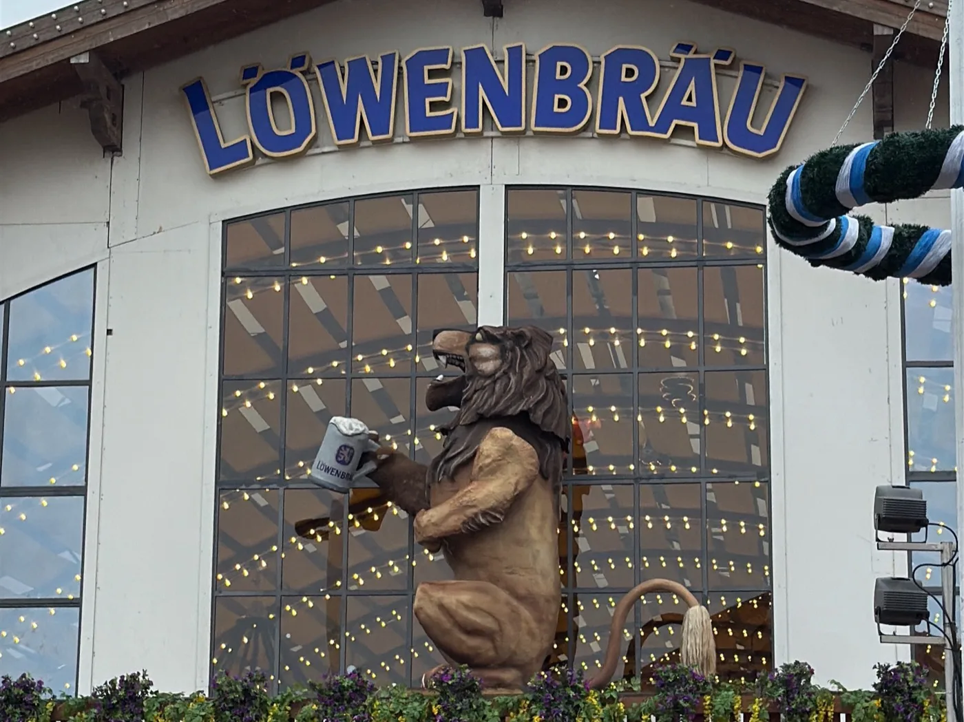 Fachada do Löwenbräu-Festzelt: o leão de 4,5 metros ergue a caneca sobre a entrada, com a placa dos Festwirte embaixo. Foto minha, setembro de 2026.